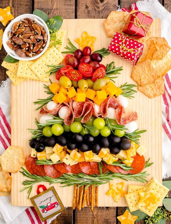 Image shows a charcuterie board shaped like a Christmas tree and decorated with small gifts and chips. via sugar and soul