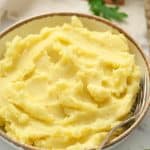 Instant Pot Mashed Potatoes served in a white dish with brown trim and a gold fork. -Skip To My Lou