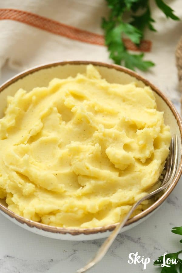 Instant Pot Mashed Potatoes served in a white dish with brown trim and a gold fork. -Skip To My Lou