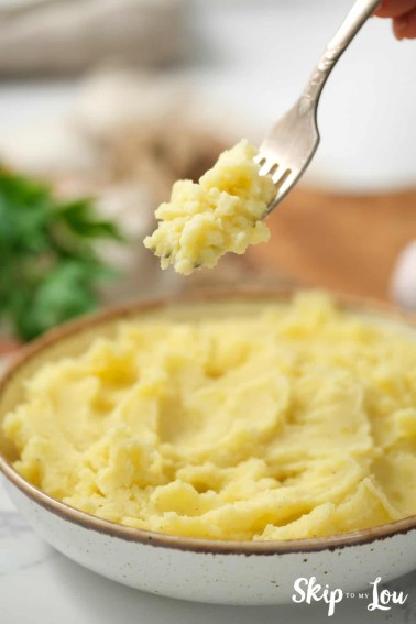 Forkful of Instant Pot mashed potatoes hovering over a large bowl of fresh mashed potatoes, by Skip to my Lou.