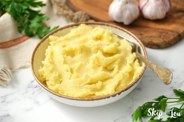 Instant Pot Mashed Potatoes mashed until smooth served in a white bowl with a brown rim. -Skip To My Lou