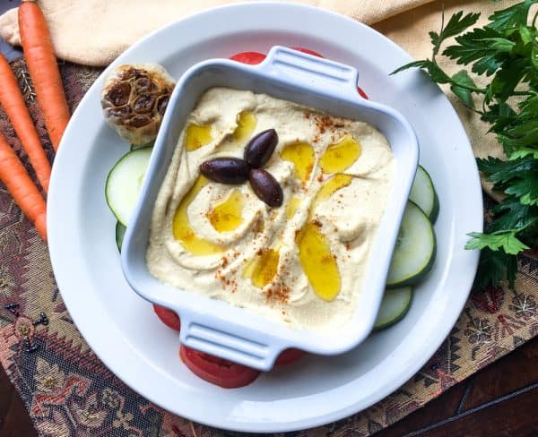 top view roasted garlic hummus in a square white bowl garnished with black olives