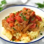 Finished Swiss Steak served over mashed potatoes in a blue rimmed white bowl. -Skip To My Lou