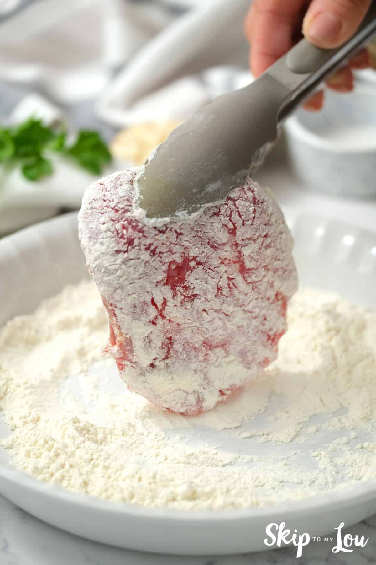 Both sides of bottom round steak dredged in flour in a white pie pan. Swiss Steak Recipe -Skip to My Lou