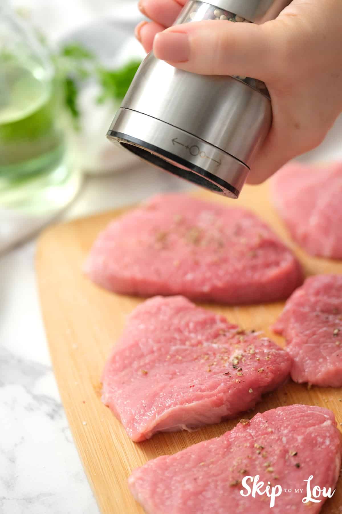 Ground pepper being put on slices of bottom round steak on a cutting board. Swiss Steak Recipe -Skip To My Lou