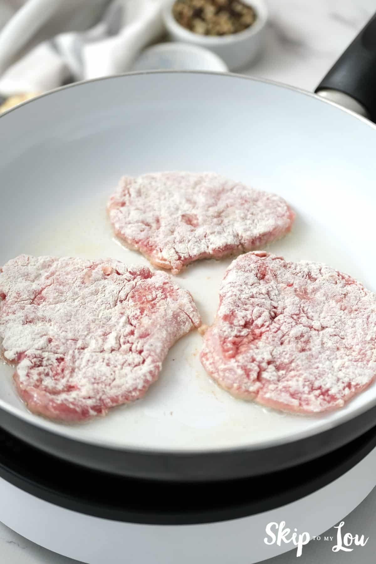 Steak being cooked in a white skillet with a small amount of vegetable oil. Swiss Steak Recipe -Skip To My Lou.