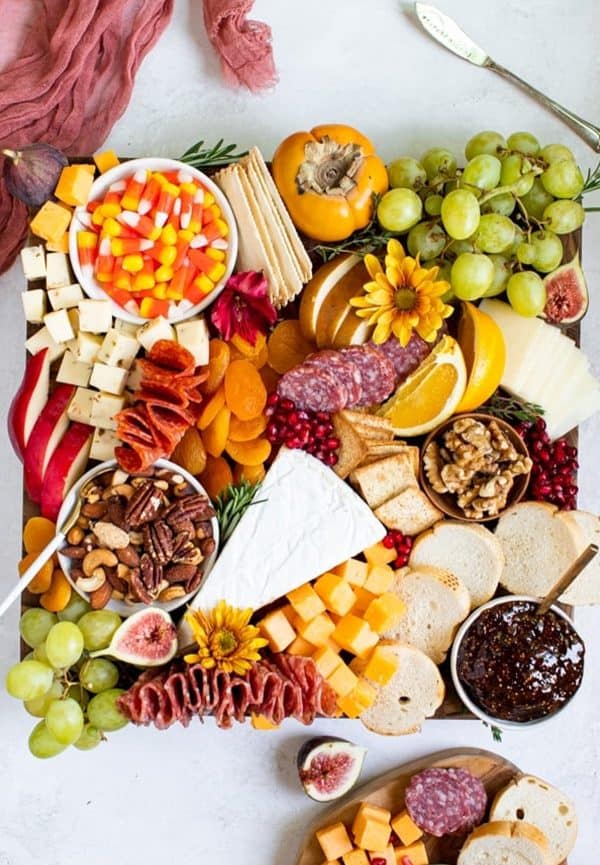 Image shows a large Thanksgiving charcuterie board with a mini pumpkin, candy corn, cheese, and more.