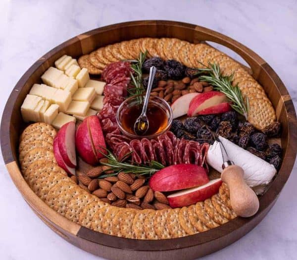 Image shows a fall / thanksgiving charcuterie board with apples, crackers, and nuts.