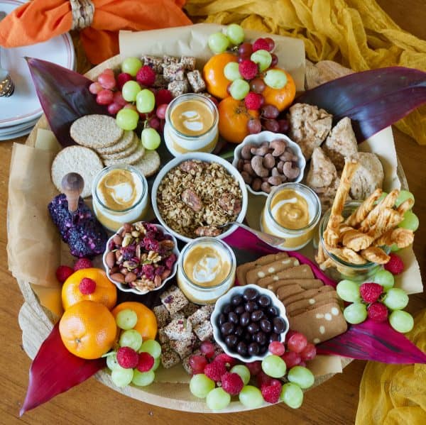Image shows a charcuterie board with crackers, grapes, oranges, etc.