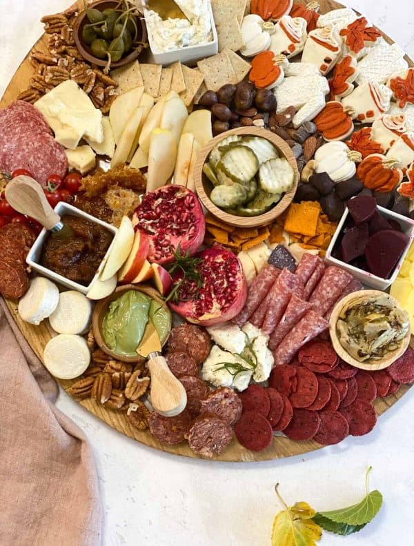 Image shows a fall charcuterie board with pumpkin dip, cookies, and other fall theme foods.