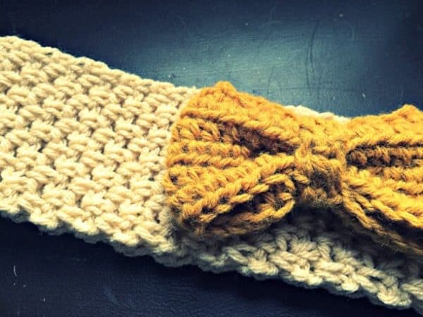 crochet ear warmer with cream yarn and yellow bow on a black table skip to my lou