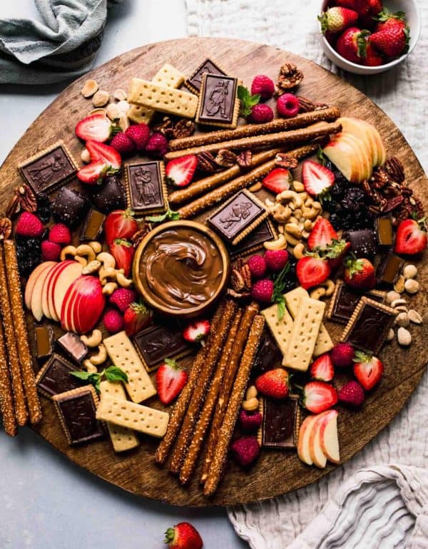 Image shows a dessert charcuterie board with chocolates, nuts, cookies, and fresh fruits. via platings & pairings