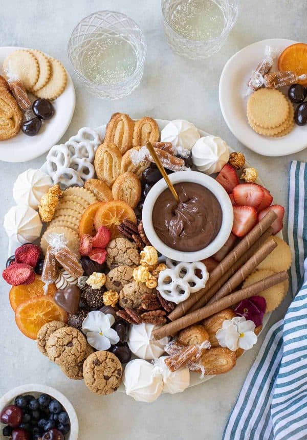 Image shows a dessert charcuterie board with cookies, meringue, dried fruit, fresh fruit, and chocolate. from sugar and charm
