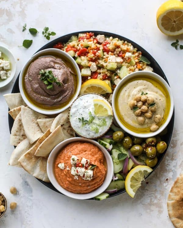 Image shows a three-dip hummus board with pita bread and gren olives.