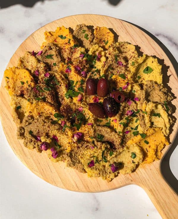 Image shows a vegan hummus board with black olives.
