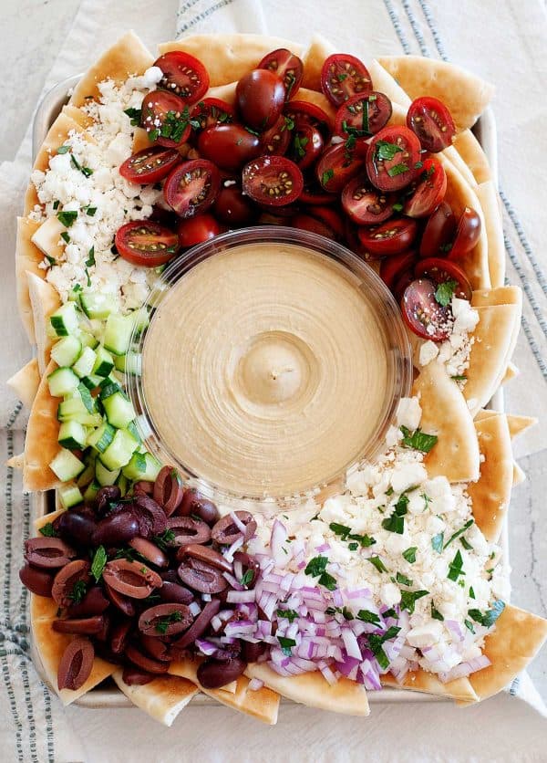 Image shows greek nachos with feta cheese, cucumber, tomatoes and a hummus dip.
