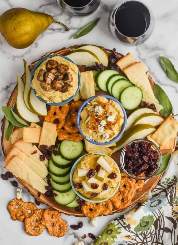 Image shows a hummus platter with cucumber, cheese, pretzels, and more ingredients.