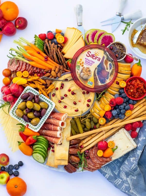 Image shows a charcuterie board with meats, herbs, and Sabra hummus.