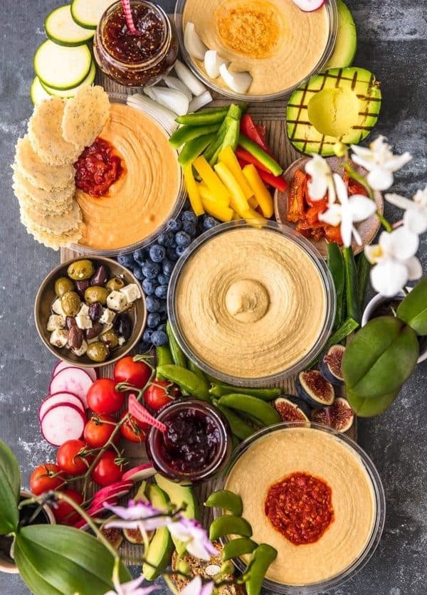 Image shows a hummus platter with fresh veggies and decorated with plants.