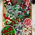 Image shows a Christmas candy charcuterie board that includes green and red candies like gummy candy, m&m's, candy cane, peppermint candies, on a wooden board. from Skip To My Lou