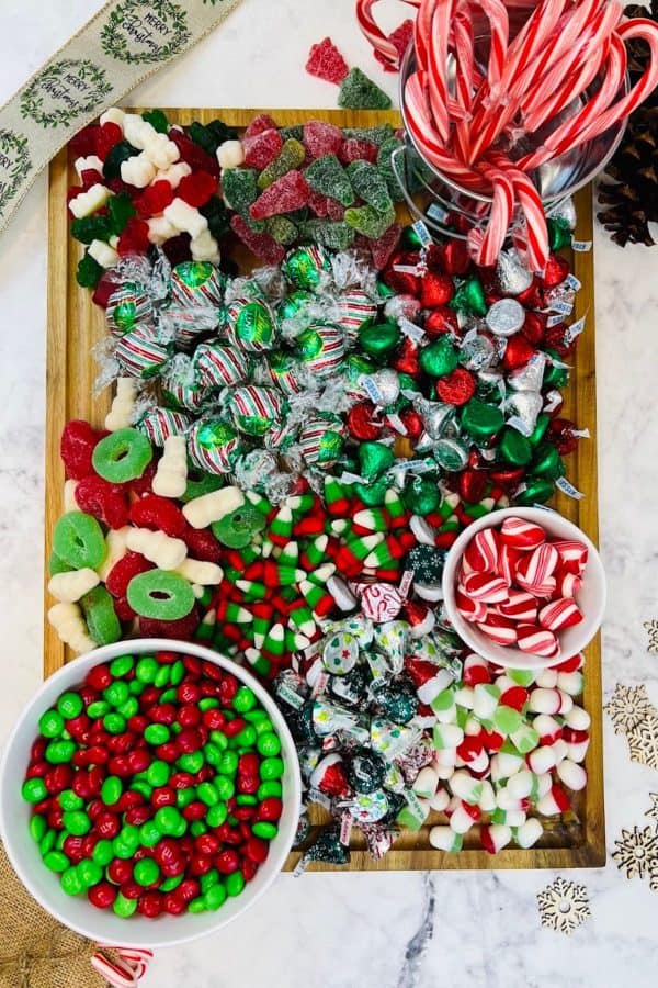 Image shows a Christmas candy charcuterie board that includes green and red candies like gummy candy, m&m's, candy cane, peppermint candies, on a wooden board. from Skip To My Lou