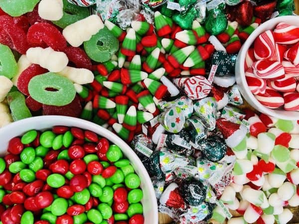 Image shows a Christmas candy charcuterie board that includes green and red candies like gummy candy, m&m's, candy cane, peppermint candies, on a wooden board. from Skip To My Lou