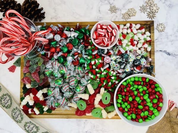 Image shows a Christmas candy charcuterie board that includes green and red candies like gummy candy, m&m's, candy cane, peppermint candies, on a wooden board. from Skip To My Lou