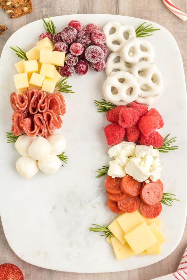 candy cane charcuterie board ideas- a board with white chocolate pretzels, cheese, meat, and rosemary garnish