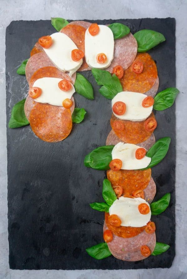 candy cane charcuterie board ideas- a board with  pepperoni, salami, and cheese topped with tomatoes and fresh basil. 