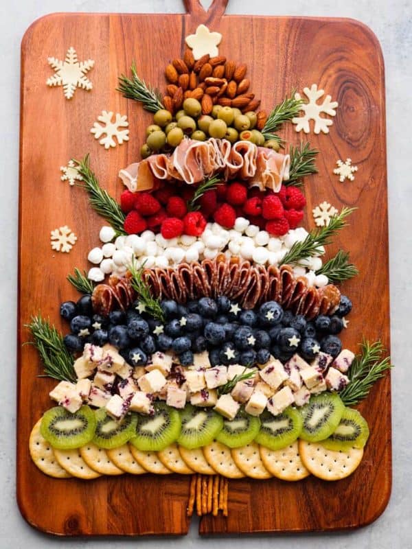 christmas tree charcuterie board ideas- kiwi, blueberries, crackers, meats, and cheeses on a cutting board.