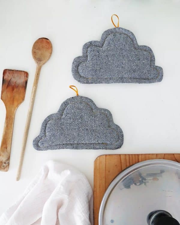 Two pot holders shaped like clouds with wooden spoons next to them.
