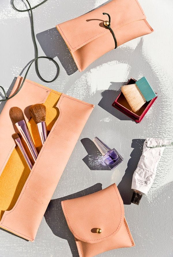 Sewn leather pouches with makeup items next to them.