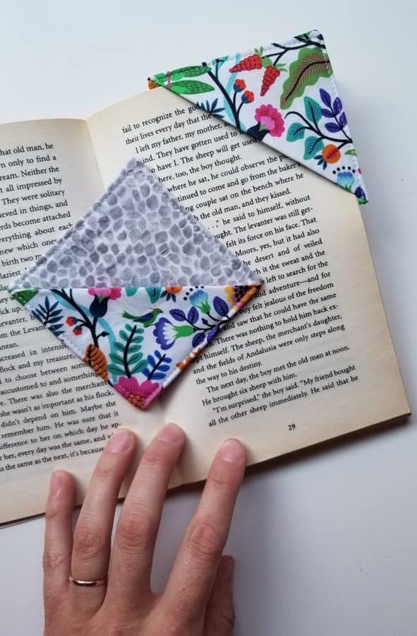 Image shows a hand with a book and fabic bookmarks.