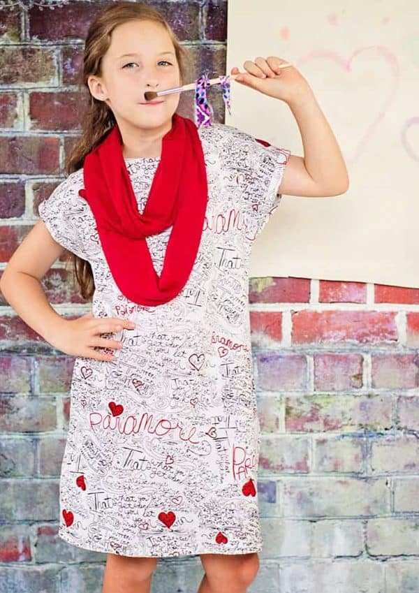 Little girl with a sewn pullover dress and a scarf standing outside.