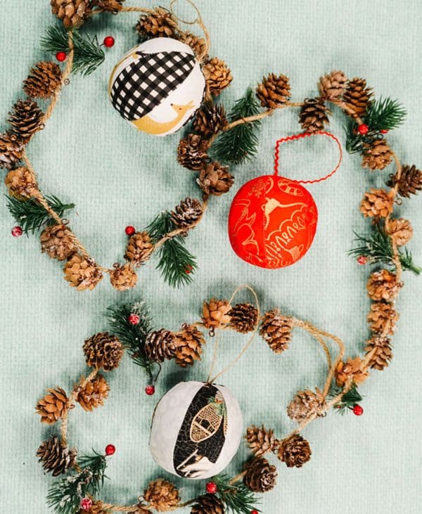 Image shows different ornament balls hanging from a wreath with pinecones.