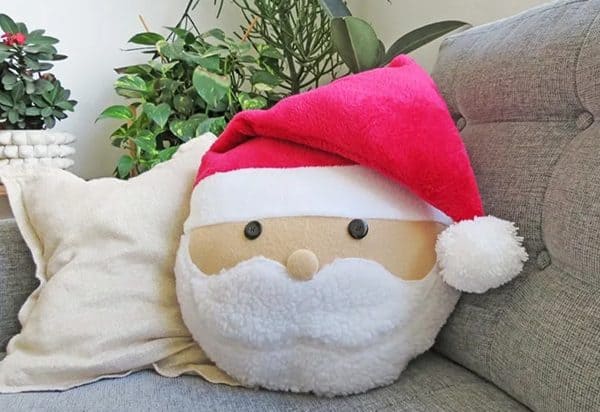 Image shows a santa pillow on a sofa in front of some plants.