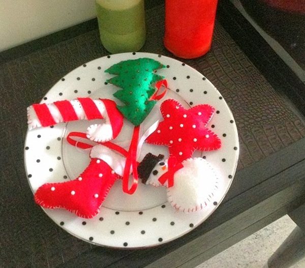 Image shows a plate with Christmas felt ornaments on top of it - a snowman, a stocking, a christmas tree, a star and a candy cane.