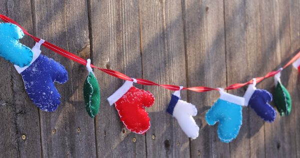 Image shows a mitten garland hanging from a wooden wall.