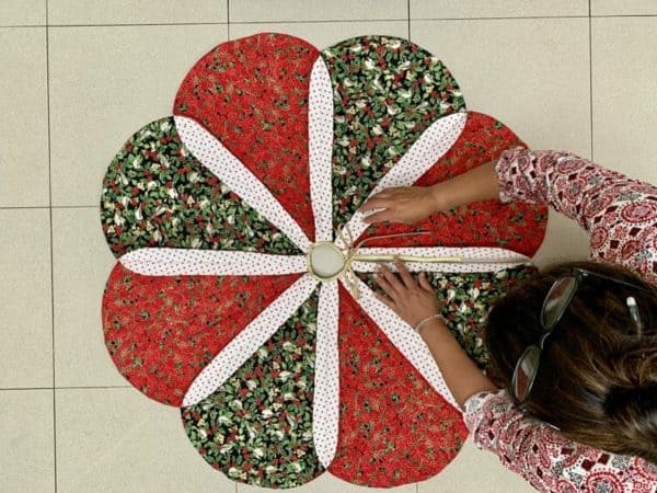 Image shows a woman putting together a christmas tree skirt with festive patterns.