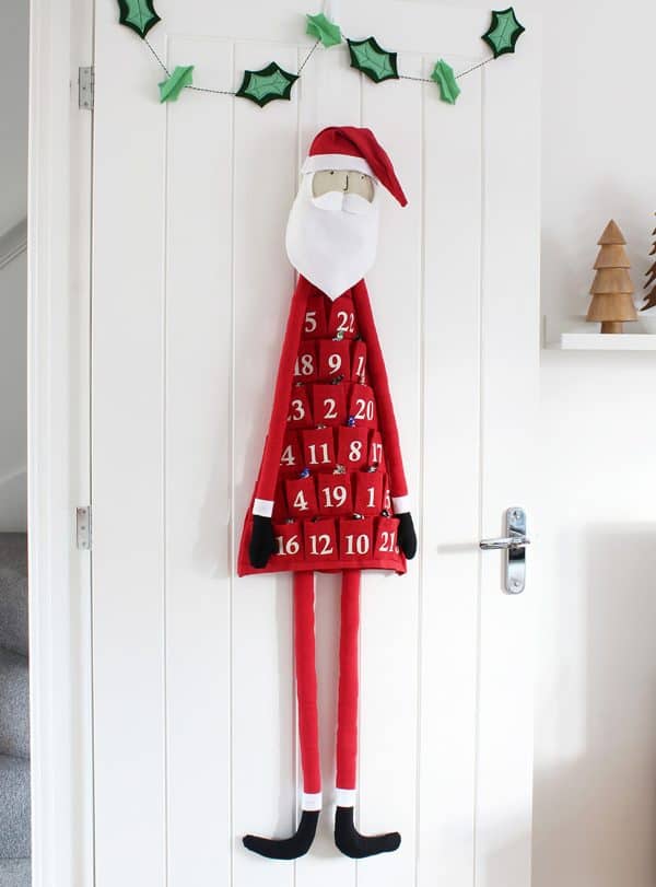 Image shows a fabric santa advent calendar hanging from a wall.