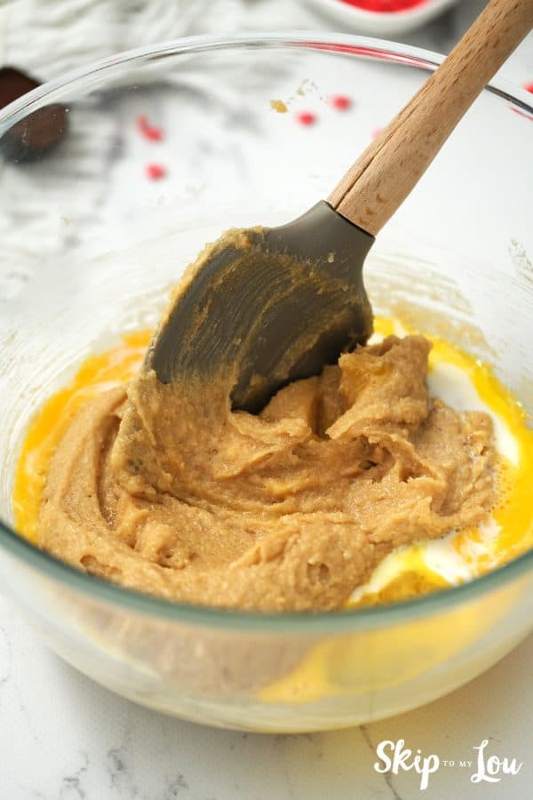 Round glass mixing bowl with peanut butter cookie dough being mixed by a black spatula, by Skip to my Lou.
