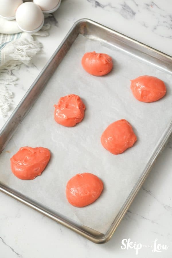 6 scoops of pink strawberry cakemix batter in rows on a parchment paper lined cookie sheet, by Skip to my Lou.