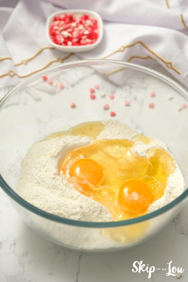 A glass mixing bowl with sugar cookie mix and two large eggs inside, by Skip to my Lou.