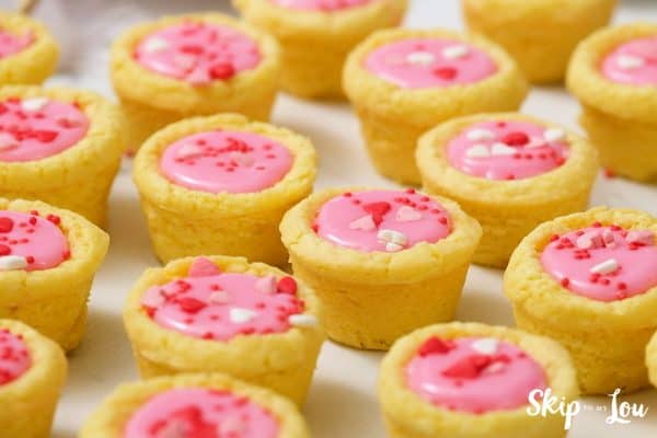Twelve Valentine Sugar Cookie cups sitting in rows on a white table, by Skip to my Lou.
