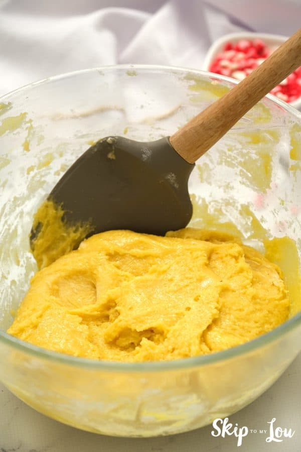 Glass mixing bowl with black rubber spatula and sugar cookie dough that has been prepared, by Skip to my Lou.