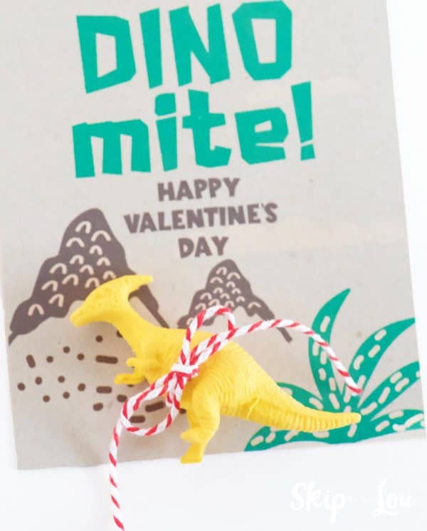 Brown card with dinosaur Valentine saying, yellow dinosaur tied to the card with red and white string, by Skip to my Lou.