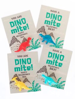 four dinosaur valentine cards with different colored plastic toy dinosaurs attached