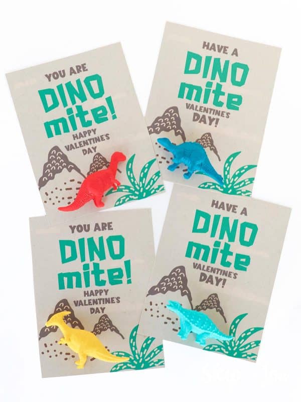 four dinosaur valentine cards with different colored plastic toy dinosaurs attached