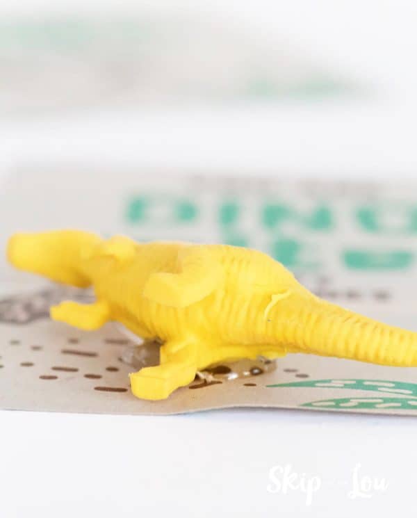 Yellow dinosaur eraser laying on its side, hot glued on dinosaur Valentine card, by Skip to my Lou.