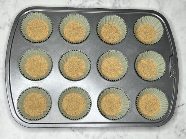 graham cracker crumbs in a layer at the bottom of cupcake liners in a pan